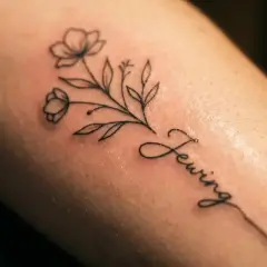 Delikatny line art tattoo z gałązką kwiatów i napisem "Sewing".