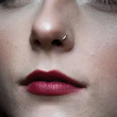Zbliżenie na twarz z ciemną szminką i subtelną wymianą kolczyka w nosie nostril.