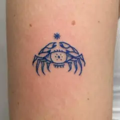 Niebieski tatuaż raka z okiem w środku, symbolizujący intuicję i ochronę.