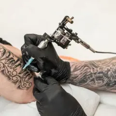 Artysta tworzy nowy tatuaż na przedramieniu klienta, używając maszynki do tatuowania.