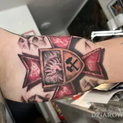 Tatuaż patriotyczny na ramieniu: lew w koronie i skrzyżowane młot i kilof na tle czerwonej gwiazdy.