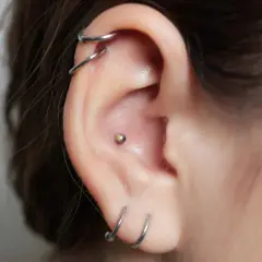 Ucho z kilkoma kolczykami, w tym subtelny orbital conch piercing z małą kuleczką.