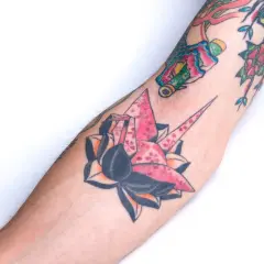 Kolorowe japońskie kwiaty tatuaże na ramieniu, w tym różowy żuraw origami ozdobiony kwitnącą wiśnią.