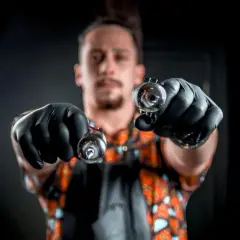 Artysta z wytatuowanymi oczami trzyma dwie maszynki do tatuażu, gotowy do stworzenia dzieła.