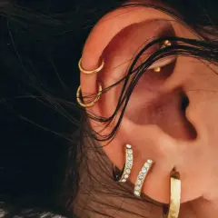 Ucho ozdobione złotymi kolczykami, w tym subtelnym conch piercingiem, podkreśla indywidualny styl.