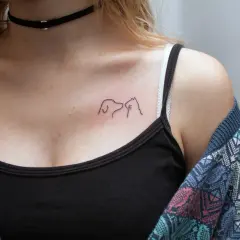 Minimalistyczny tatuaż pies i kot na dekolcie, symbol przyjaźni między gatunkami.