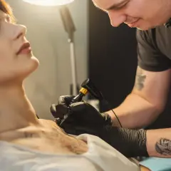 Artysta tworzy tatuaż grupy krwi na szyi kobiety.