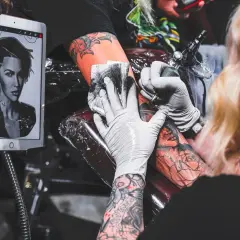 Artysta przemywa tatuaż podczas pracy, korzystając z wzoru na tablecie.