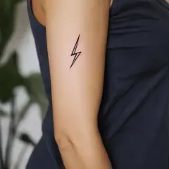 Minimalistyczny tatuaż piorun na ramieniu kobiety. Symbolizuje moc i energię.