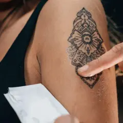 Delikatne gojenie tatuażu bez folii. Palec rozsmarowuje maść na świeżym wzorze na ramieniu.