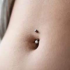 Zbliżenie na brzuch z kolczykiem w pępku. Delikatna skóra, subtelny blask biżuterii. To jest właśnie ten słynny **angie piercing**.