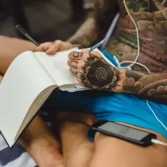 Artysta z ręką ozdobioną tatuażem w stylu japońskim szkicuje w notatniku, inspirując się własnym ciałem pokrytym wzorami.