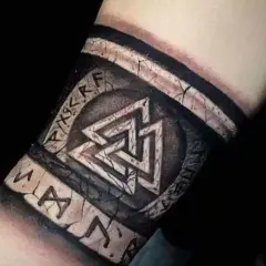 Tatuaż na przedramieniu z nordyckimi symbolami: Valhalla i runy. Wygląda jak starożytny artefakt.