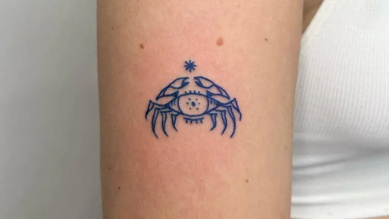 Niebieski tatuaż raka z okiem w środku, symbolizujący intuicję i ochronę.