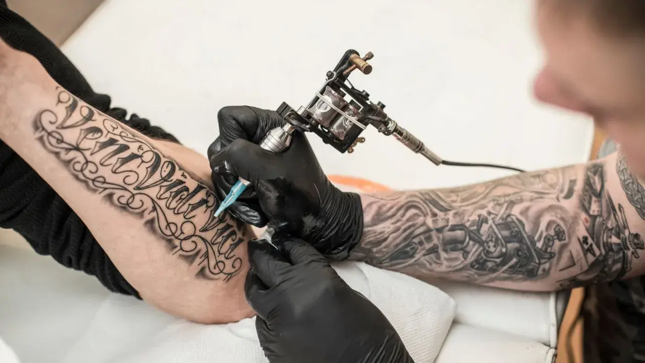 Artysta tworzy nowy tatuaż na przedramieniu klienta, używając maszynki do tatuowania.