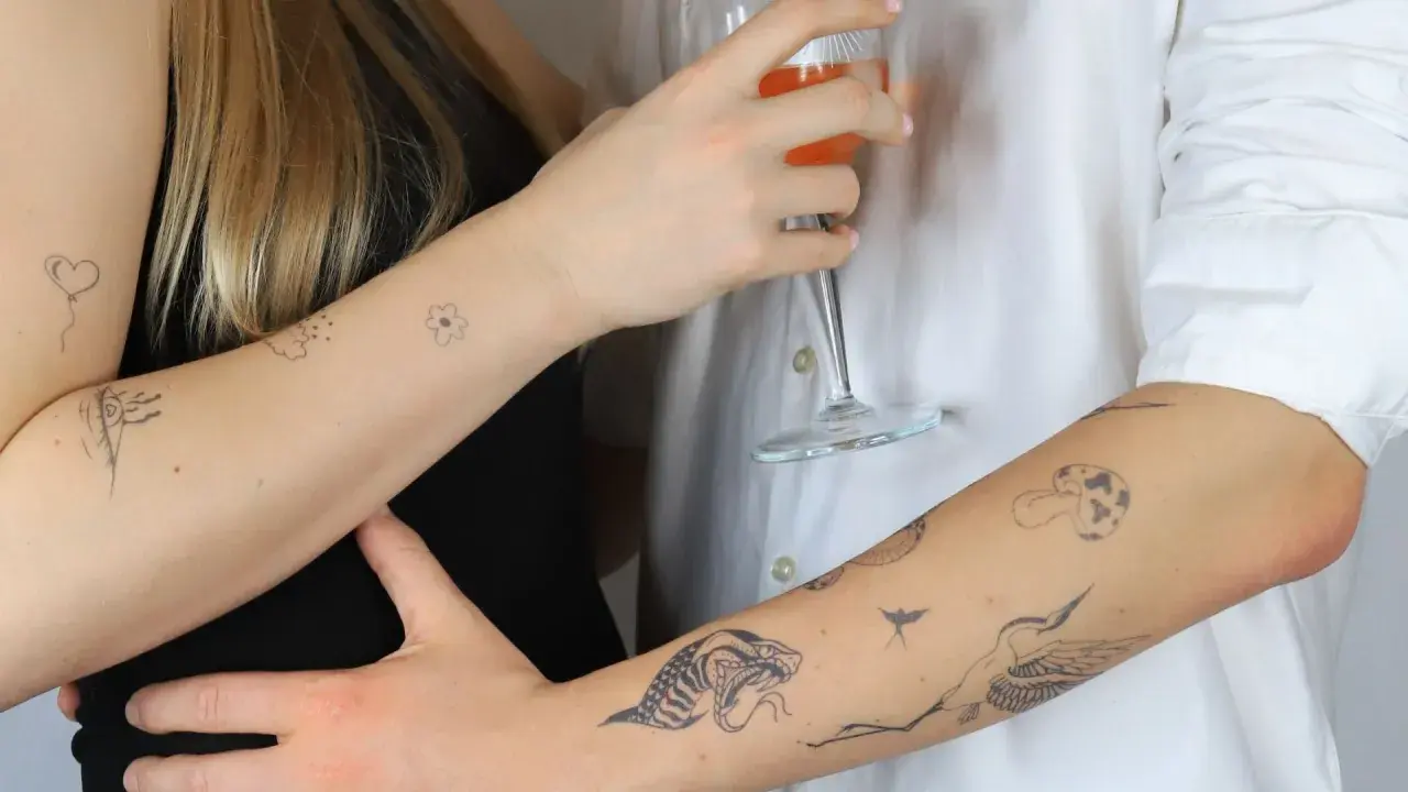 Dłonie z delikatnymi tatuażami: serce, kwiat, oko, wąż, żuraw. Subtelny ornament tattoo na skórze.