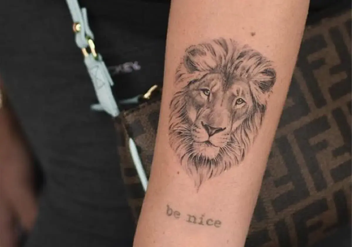 Tatuaż znak zodiaku lew na ramieniu, z napisem "be nice" poniżej.