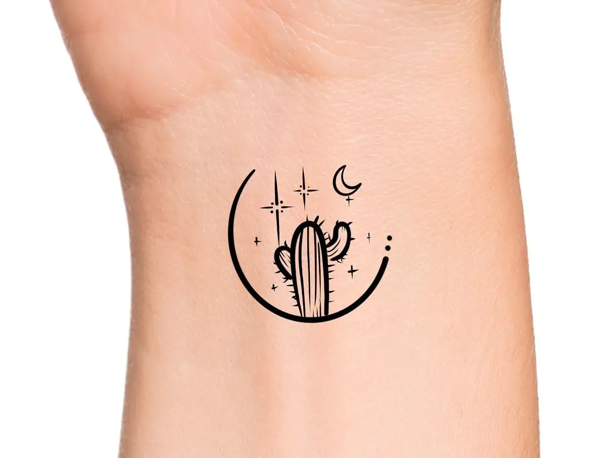 Minimalistyczny kaktus tatuaz na nadgarstku, otoczony księżycem i gwiazdami.