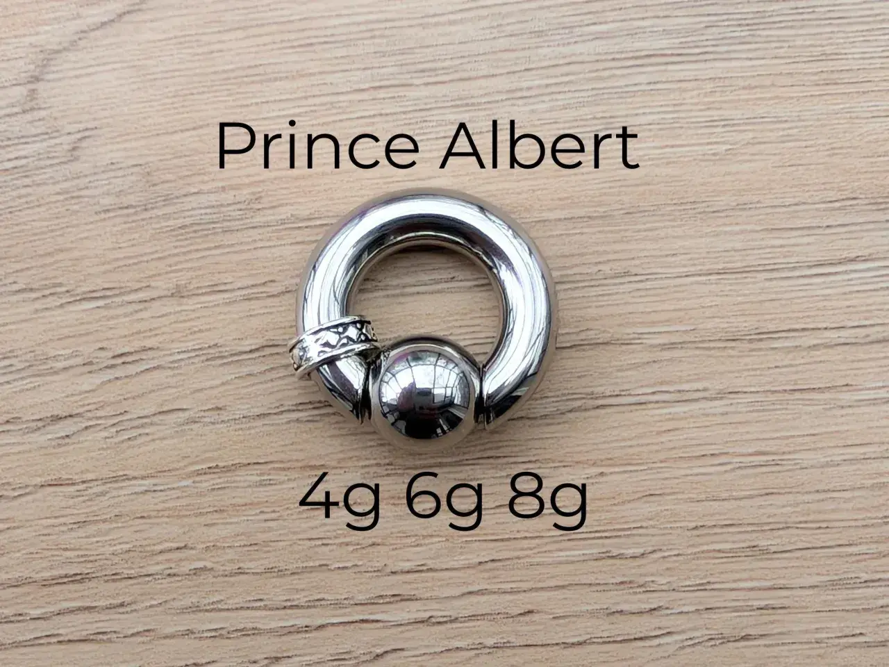Stalowy kolczyk typu prince albert, z kulką i ozdobnym pierścieniem, rozmiary 4g, 6g, 8g.