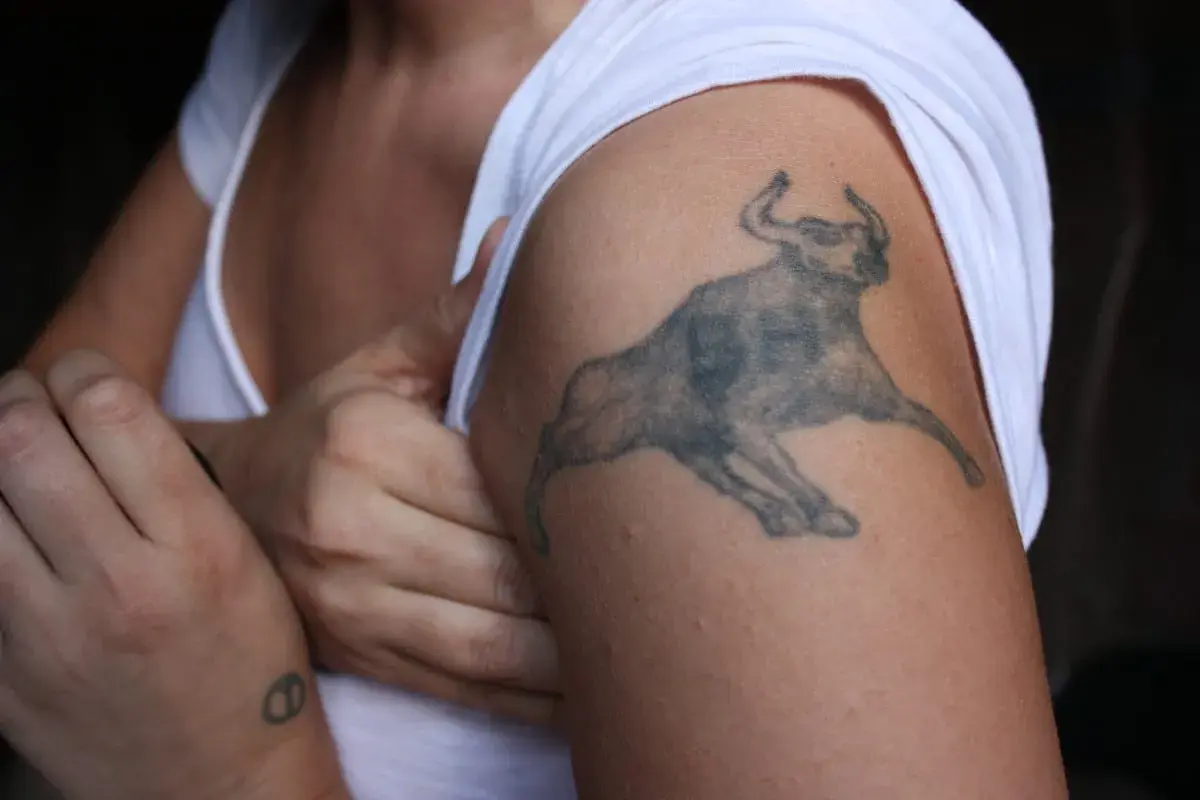 Tatuaż byk na ramieniu, symbol siły i determinacji. Obok mały tatuaż na nadgarstku.