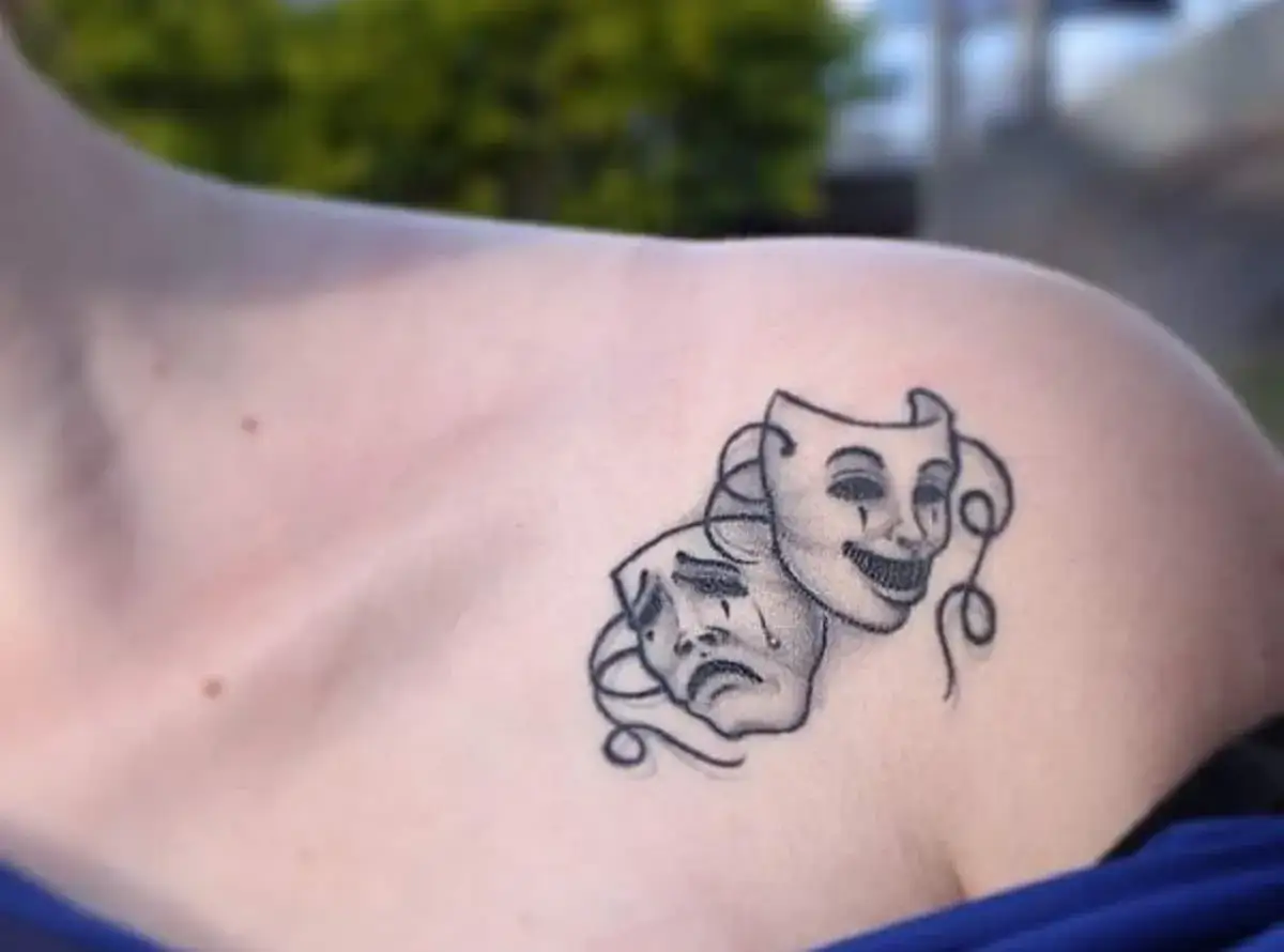 Smutne tatuaże przedstawiające maski komedii i tragedii, symbolizujące zmienność nastrojów i ukrywanie emocji.