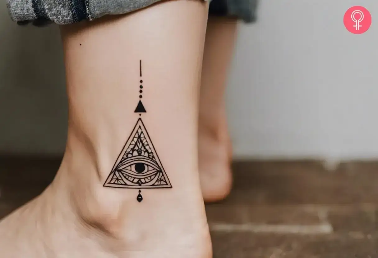 Delikatny tatuaż na kostce, przedstawiający oko opatrzności w trójkącie, symbolizujący tajemnicę i wiedzę. To subtelny tatuaż illuminati.